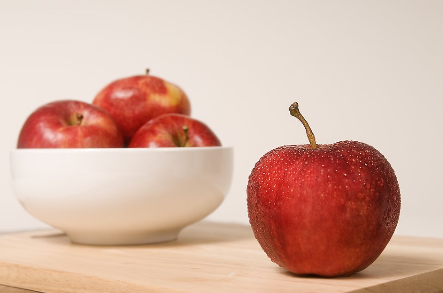 a bowl of red apples on a chopping board